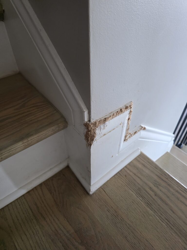 Damaged baseboard trim and stair trim before repair